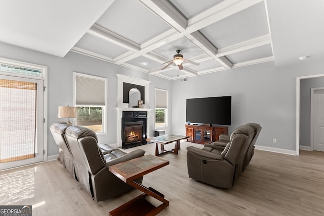 living area with coffered ceiling, baseboards, light wood-type flooring, beamed ceiling, and a glass covered fireplace