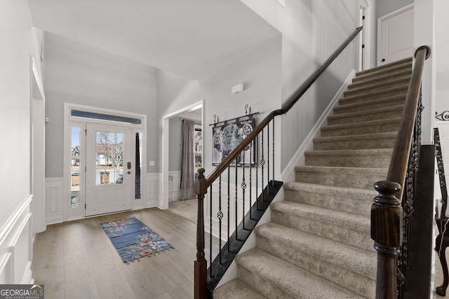 entrance foyer featuring light wood-style floors, stairway, a decorative wall, and a wainscoted wall