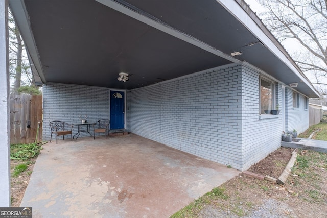 exterior space with a carport, brick siding, a patio, and fence