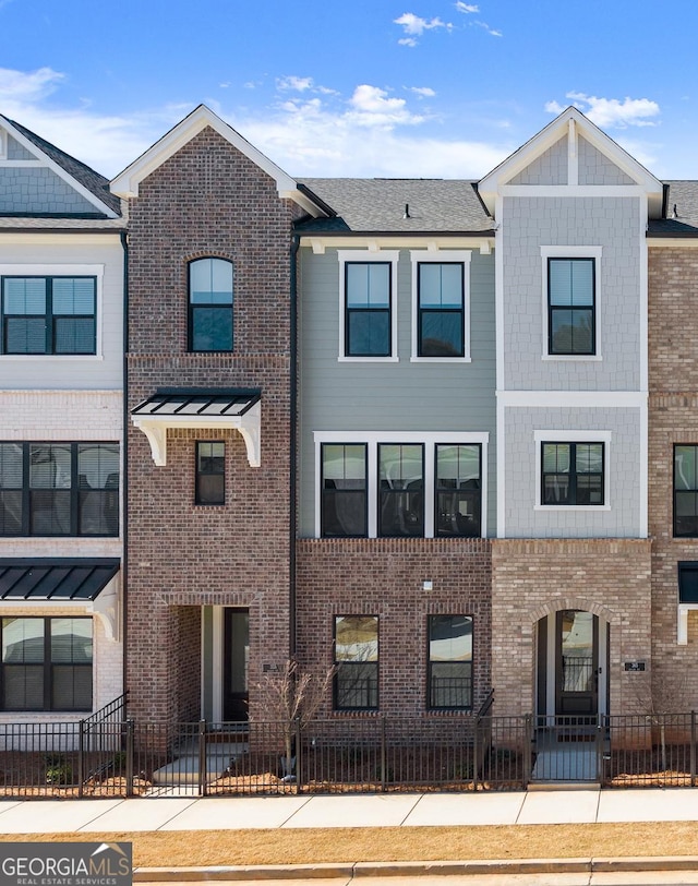 townhome / multi-family property featuring a fenced front yard and brick siding