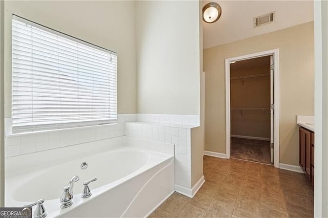 full bath featuring a bath, visible vents, vanity, baseboards, and a spacious closet