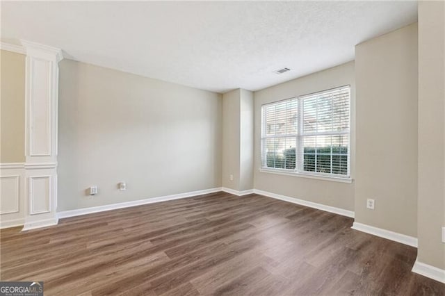 empty room featuring baseboards, visible vents, and dark wood-type flooring