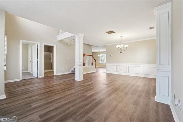 unfurnished living room featuring visible vents, stairs, wood finished floors, a notable chandelier, and ornate columns