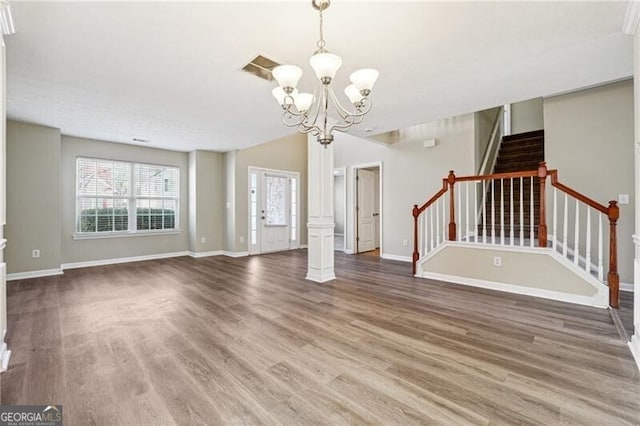 unfurnished living room featuring baseboards, a notable chandelier, wood finished floors, and stairway