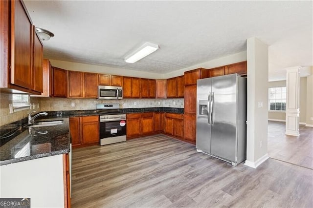 kitchen with decorative backsplash, decorative columns, a sink, light wood finished floors, and stainless steel appliances