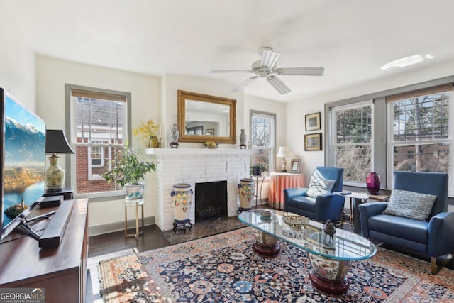 living area featuring a brick fireplace, a healthy amount of sunlight, ceiling fan, and baseboards