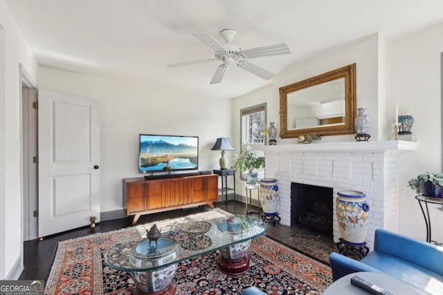 living room with a brick fireplace, a ceiling fan, baseboards, and dark wood-type flooring