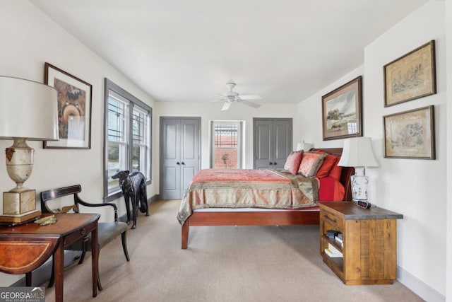 bedroom with light carpet, ceiling fan, baseboards, and two closets