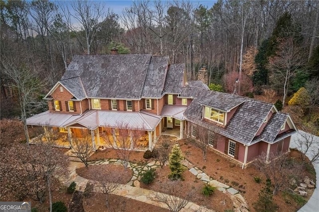 view of front of property featuring brick siding, a chimney, and a view of trees