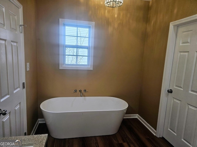 bathroom featuring a freestanding tub, baseboards, and wood finished floors