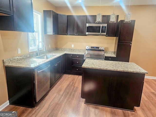 kitchen featuring stainless steel appliances, a sink, light wood-style floors, light stone countertops, and decorative light fixtures