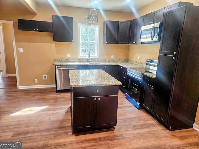 kitchen with a sink, appliances with stainless steel finishes, a center island, light wood finished floors, and decorative light fixtures