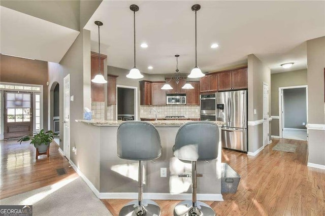 kitchen featuring tasteful backsplash, arched walkways, appliances with stainless steel finishes, a peninsula, and hanging light fixtures