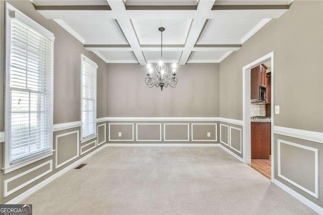 unfurnished dining area featuring a chandelier, light colored carpet, coffered ceiling, visible vents, and beam ceiling