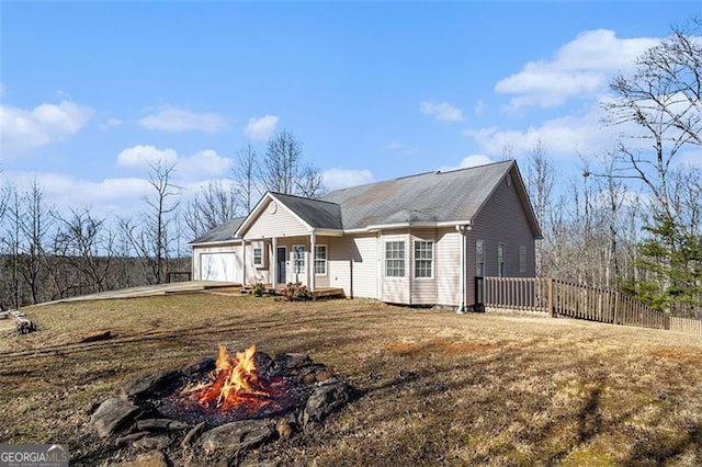 ranch-style home featuring an attached garage, an outdoor fire pit, fence, and a front lawn