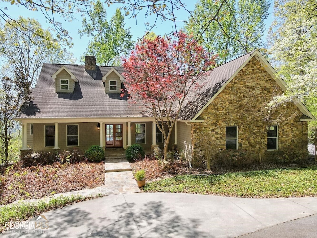 cape cod home featuring french doors, stone siding, and a chimney