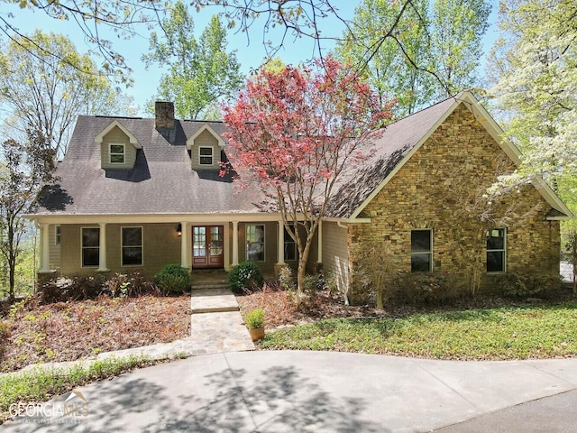 cape cod home featuring french doors, stone siding, and a chimney