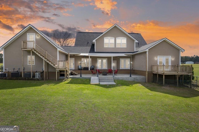 back of house at dusk featuring french doors, a yard, a patio, stairway, and central AC