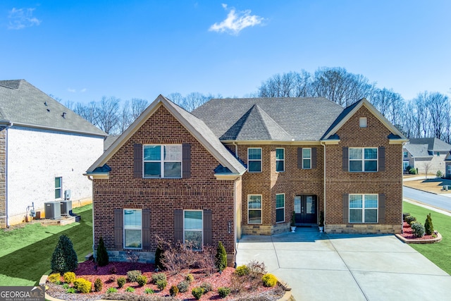 view of front of home featuring brick siding, roof with shingles, a front yard, and central air condition unit