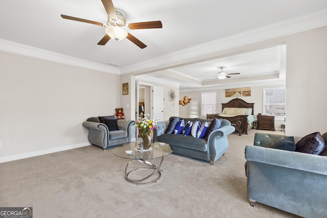 living room featuring light carpet, a ceiling fan, baseboards, ornamental molding, and a tray ceiling