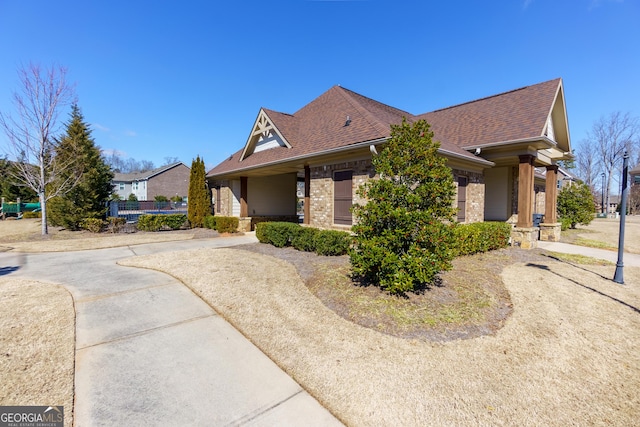 view of front of house with a shingled roof, brick siding, and fence