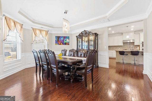 dining area with dark wood finished floors, a wainscoted wall, a tray ceiling, crown molding, and a decorative wall