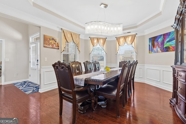 dining space with a decorative wall, ornamental molding, a tray ceiling, dark wood finished floors, and an inviting chandelier