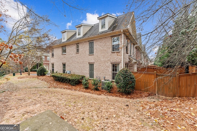 view of property exterior with central air condition unit, fence, and brick siding