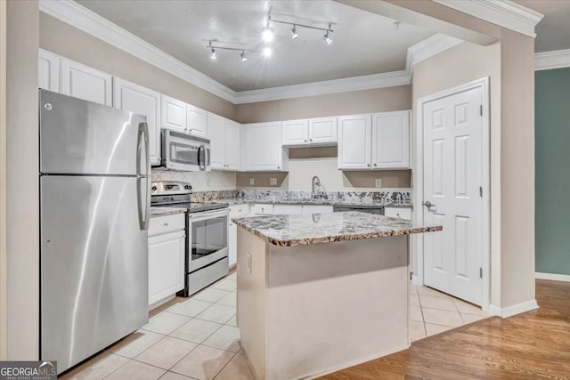 kitchen with light tile patterned floors, ornamental molding, a center island, stainless steel appliances, and white cabinetry