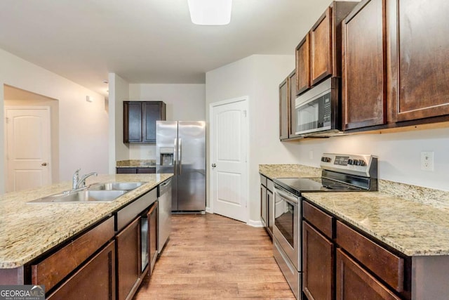 kitchen with stainless steel appliances, a sink, dark brown cabinets, light wood-type flooring, and an island with sink