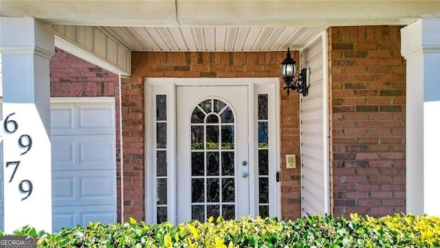 doorway to property featuring a garage and brick siding