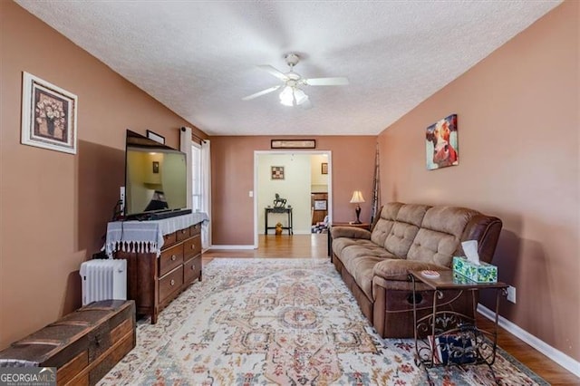 living area with a textured ceiling, ceiling fan, light wood-style flooring, baseboards, and radiator