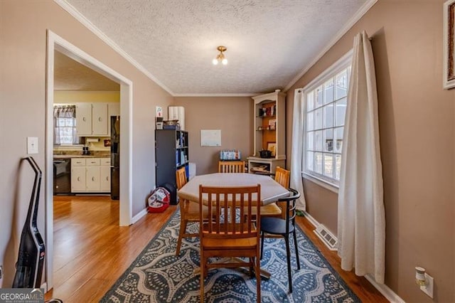 dining room with visible vents, crown molding, a textured ceiling, and light wood finished floors