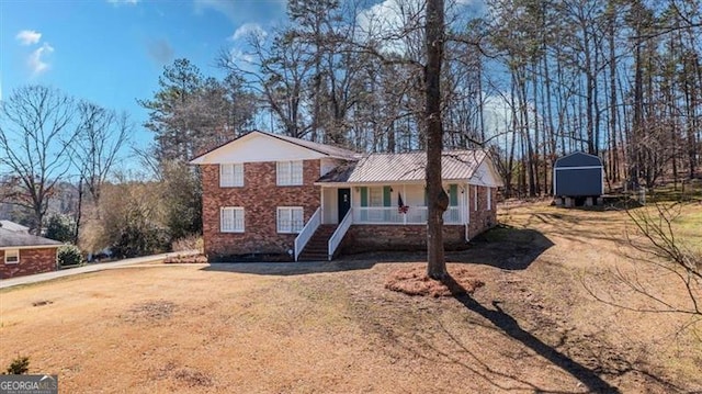 split level home with covered porch, brick siding, metal roof, and a front lawn