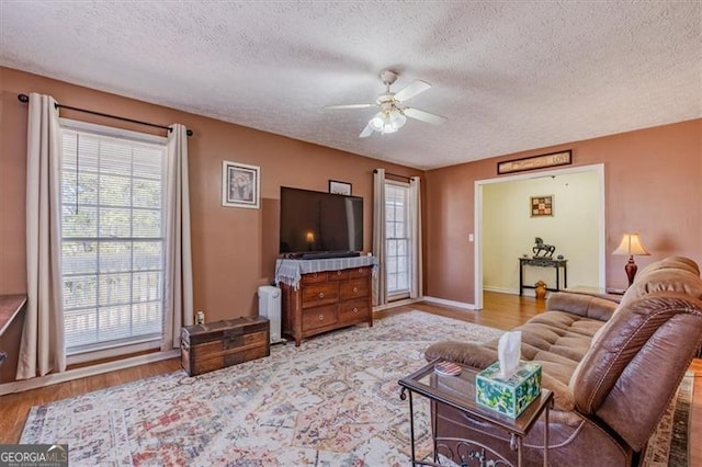 living area with light wood-style floors, a textured ceiling, and a ceiling fan