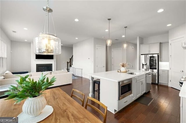 kitchen with a center island with sink, stainless steel appliances, light countertops, hanging light fixtures, and open floor plan