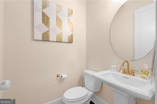 half bathroom featuring baseboards, a sink, and toilet