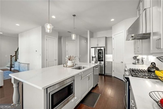 kitchen with decorative light fixtures, stainless steel appliances, a sink, wall chimney range hood, and an island with sink