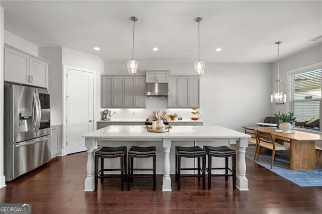 kitchen with under cabinet range hood, a breakfast bar, light countertops, stainless steel fridge with ice dispenser, and pendant lighting