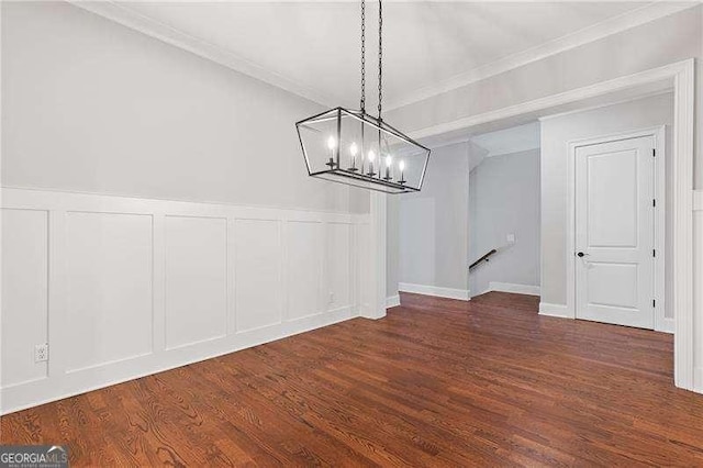 unfurnished dining area with an inviting chandelier, ornamental molding, a decorative wall, and dark wood-style flooring