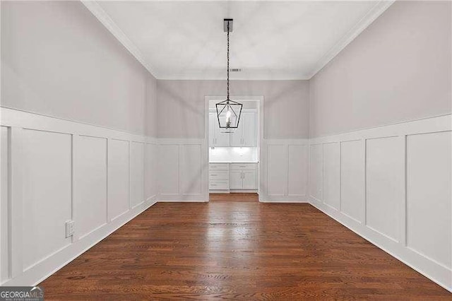 unfurnished dining area featuring crown molding, dark wood finished floors, a wainscoted wall, and a decorative wall