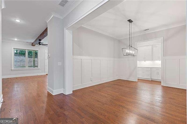 unfurnished dining area with a decorative wall, ceiling fan with notable chandelier, wood finished floors, ornamental molding, and wainscoting