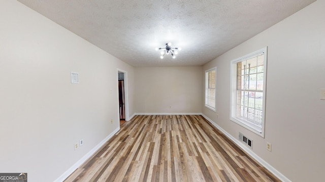 empty room featuring a textured ceiling, baseboards, visible vents, and light wood-style floors