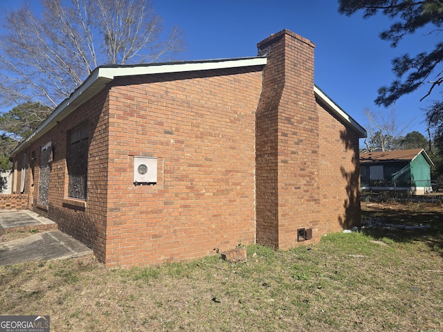 view of side of home featuring a yard, a chimney, and brick siding