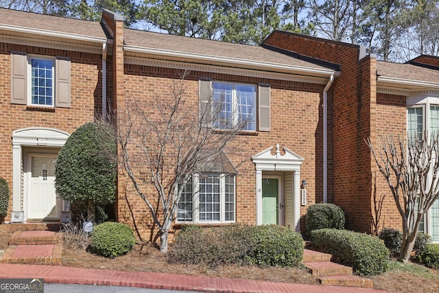 view of property featuring a shingled roof and brick siding