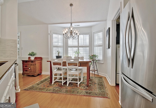 dining room featuring a healthy amount of sunlight, light wood-style floors, a textured ceiling, and a notable chandelier