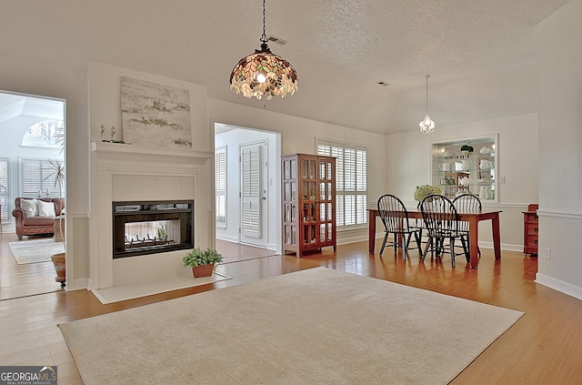 dining area with lofted ceiling, a textured ceiling, wood finished floors, and a tiled fireplace