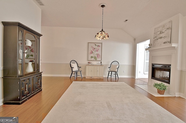 dining space with a fireplace, visible vents, vaulted ceiling, and wood finished floors