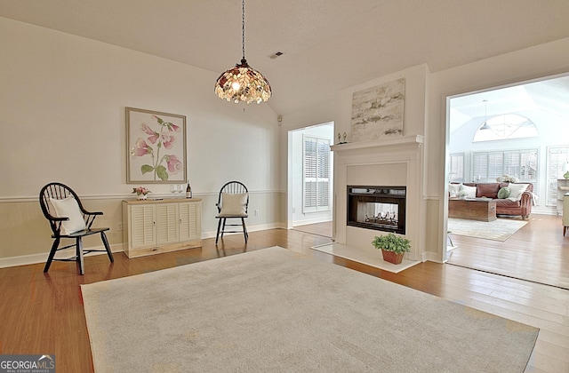 sitting room with lofted ceiling, visible vents, wood finished floors, and a multi sided fireplace