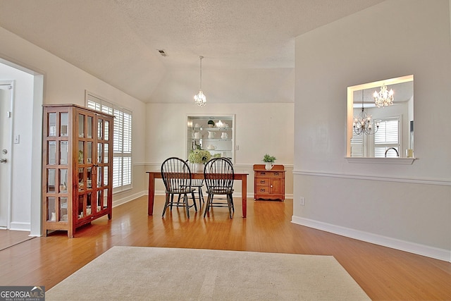 dining area with lofted ceiling, a healthy amount of sunlight, wood finished floors, and an inviting chandelier